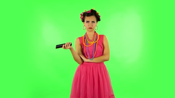 Woman with TV remote in her hand, switching on TV. Green screen — Stock Video