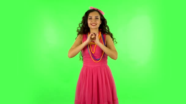 Cute girl smiles and showing heart with fingers then blowing kiss at studio. Green screen — Stockvideo