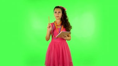 Girl stands and thinks, then writes with pencil in notebook and gets angry. Green screen
