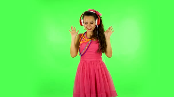 Девушка танцует и поет в больших красных наушниках на зеленом экране — стоковое видео