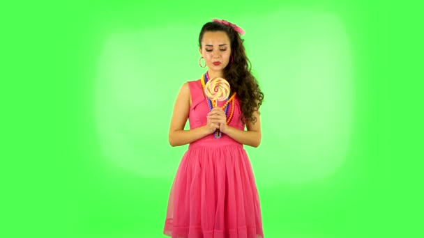 Girl with great pleasure eats a large multi-colored candy while enjoying. Green screen — Stock Video