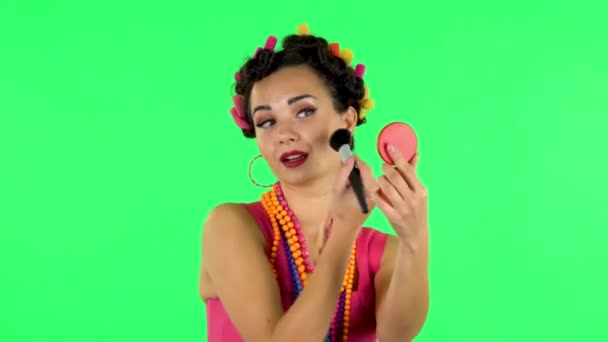 Girl with curlers on her head in a pink dress looking in red mirror and powdered her nose with big brush. Green screen — Αρχείο Βίντεο