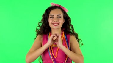 Cute girl smiles and showing heart with fingers then blowing kiss at studio. Green screen