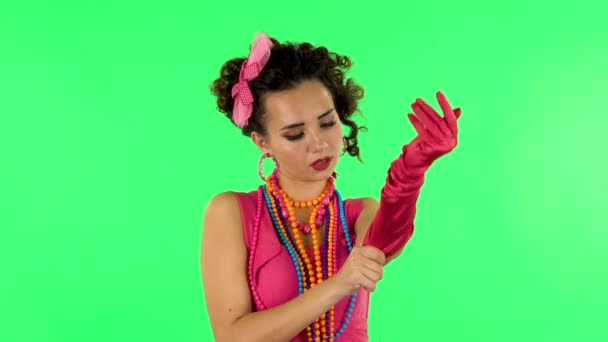 Attractive girl puts on her gloves and throws nearby on green screen — Stockvideo