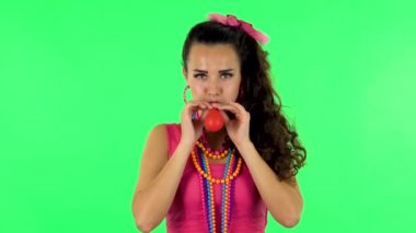 Curly girl inflates a bright red ball then rejoicing. Green screen