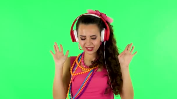 Girl dancing and singing in big red headphones on green screen — Stok video