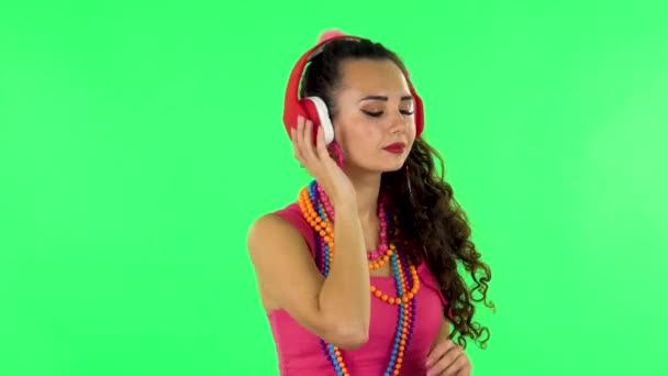 쾌활 한 소녀는 커다란 빨간 헤드폰을 끼고 춤을 추며 음악을 즐긴다. 녹색 화면 — 비디오