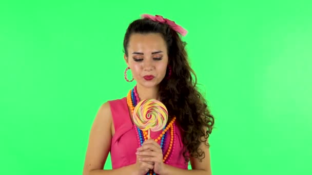 Дівчина з великим задоволенням їсть велику різнокольорову цукерку, насолоджуючись. Зелений екран — стокове відео