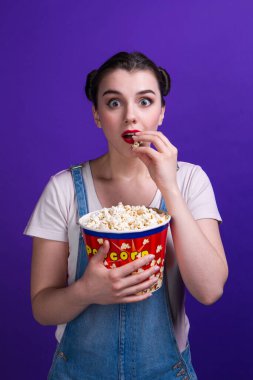 İki poposu olan harika bir kız TV şovu izler ve patlamış mısır yer ağzı açık, heyecan verici bir hikaye, izole edilmiş menekşe arkaplanı