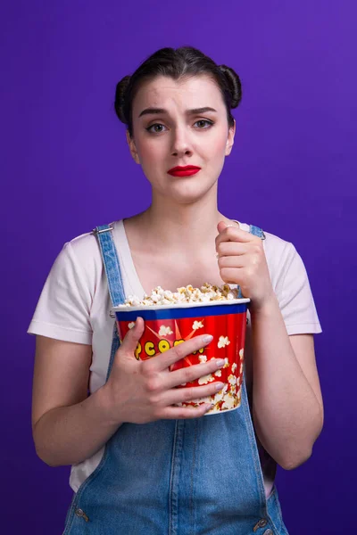 Mooie dame holding popcorn container kijken dramatische film dragen casual outfit geïsoleerd op paarse achtergrond — Stockfoto