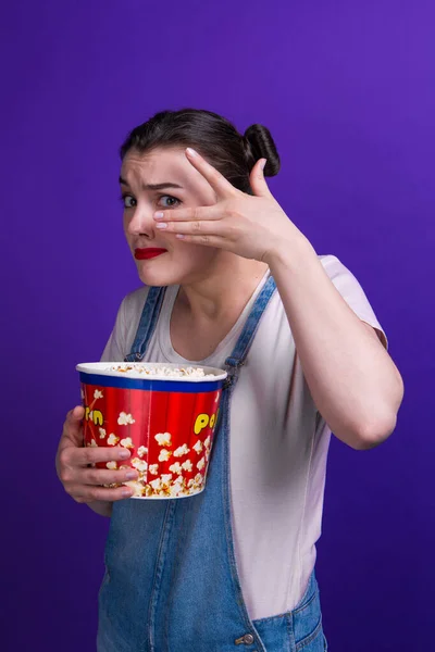 Mooie dame holding popcorn container kijken horror film dragen casual outfit geïsoleerd op paarse achtergrond — Stockfoto
