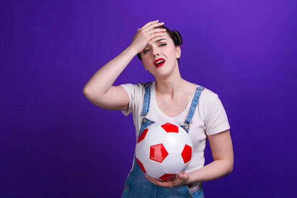 Jovem intrigada fã de futebol assistindo jogo apoio favorito equipe com bola de futebol, isolado no fundo azul . — Fotografia de Stock