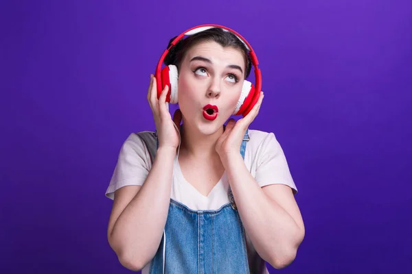 面白いです女の子歌で大きな赤いヘッドフォン隔離で青背景上のスタジオ. — ストック写真