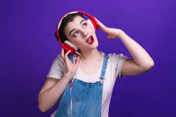 Divertente ragazza che canta in grandi cuffie rosse isolate su sfondo blu su studio . — Foto Stock