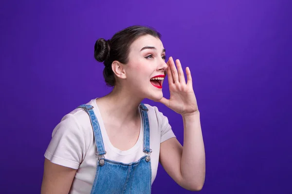 Portret van mooie jonge vrouw roepen voor iemand met de hand op haar mond over paarse achtergrond — Stockfoto