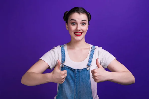 Portrait of young woman shows a Like sign on purple background at studio — Stock Photo, Image