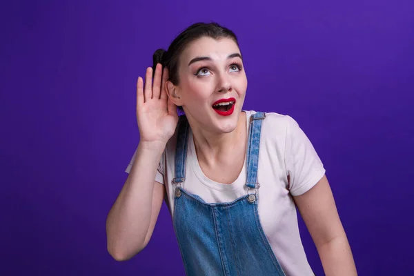 Wow žena drží ruku u ucha snaží se poslouchat zajímavé zprávy vyjadřující komunikační koncept a drby izolované přes fialové pozadí. — Stock fotografie