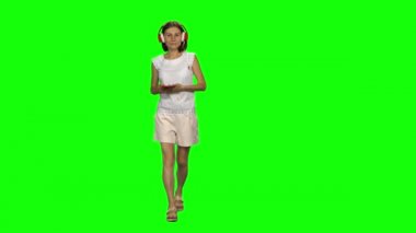 Genç kadın sakince büyük kırmızı kulaklıklarla yürüyor, yeşil ekranda cep telefonundan müzik seçiyor. Ön görünüm.