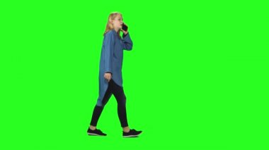 Sarışın genç kız yeşil ekrandaki cep telefonunda sakince yürüyor ve konuşuyor. Krom anahtar, 4km 'lik atış. Profil görünümü.