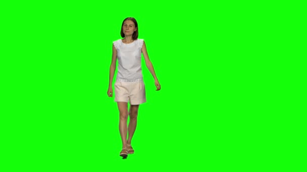 Mujer joven con el pelo castaño y corte de pelo suave está caminando tranquilamente en la pantalla verde. Tecla de croma, tiro de 4k. Vista frontal . — Vídeos de Stock