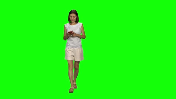 Mujer joven está tranquilamente caminando y mensaje de texto compiten su teléfono móvil en la pantalla verde. Vista frontal . — Vídeos de Stock