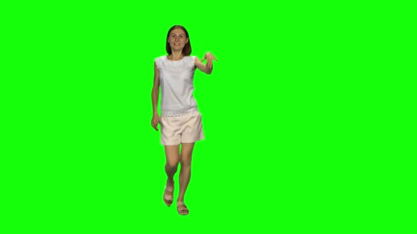 Jonge vrouw met bruin haar en glad kapsel loopt en zwaaiende hand stop op groen scherm. Chroma sleutel. Vooraanzicht. — Stockvideo