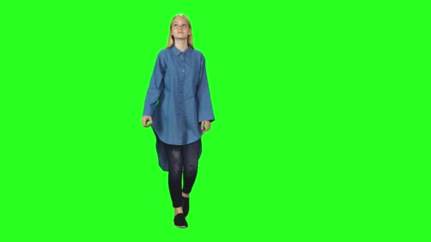 금발의 십 대 소녀는 침착하게 녹색 화면을 배경으로 걷는다. 크로마 키 , 4k 샷. 앞모습. — 비디오