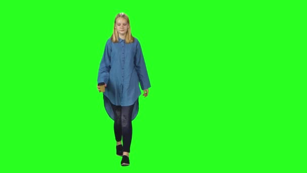 Blonde teenager girl calmly walking on green screen background. Chroma key, 4k shot. Front view. — Stock Video