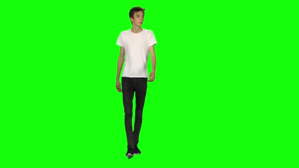 Високий худий хлопець підліток спокійно ходить на зеленому тлі екрану. Клавіша Chroma, 4k постріл. Вид спереду . — стокове відео