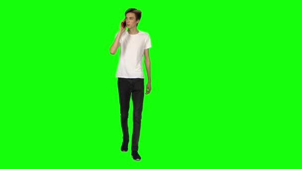 Високий худий підліток спокійно ходить і розмовляє на мобільному телефоні на зеленому екрані. Клавіша Chroma, 4k постріл. Вид спереду . — стокове відео