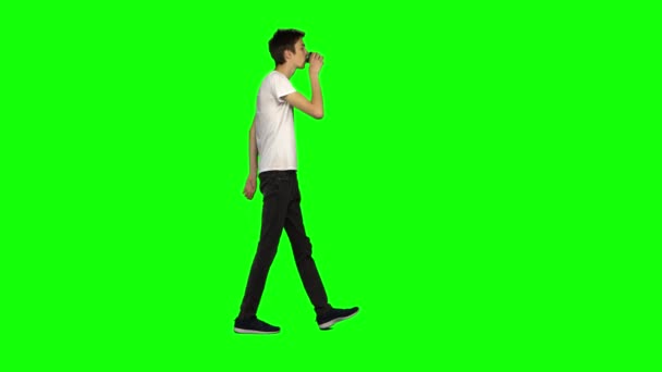 Uzun, sıska genç adam yeşil ekranda sakince yürüyor ve kahve içiyor. Krom anahtar, 4km 'lik atış. Profil görünümü. — Stok video