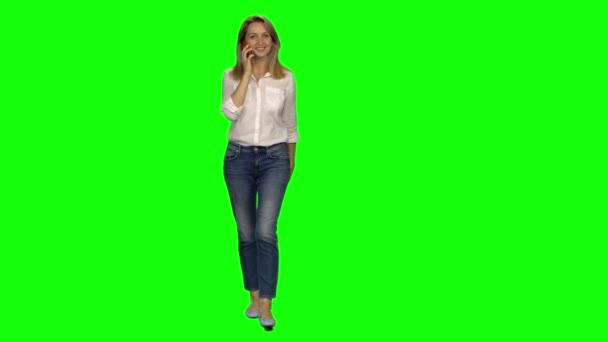 Mulher loira está calmamente andando e falando no celular na tela verde. Chave Chroma, tiro 4K. Vista frontal . — Vídeo de Stock