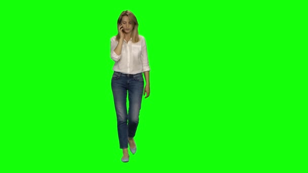 Mulher loira está calmamente andando e falando no celular na tela verde. Chave Chroma, tiro 4K. Vista frontal . — Vídeo de Stock