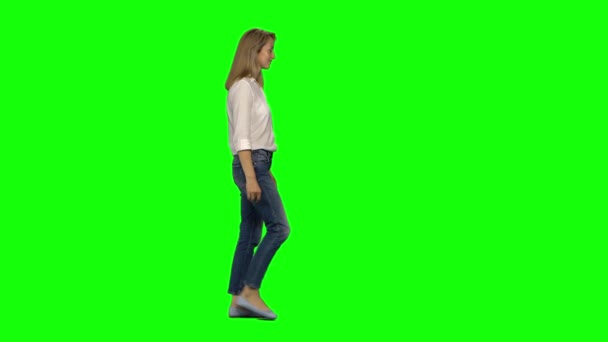 Mujer rubia está tranquilamente caminando y sonriendo en la pantalla verde. Tecla de croma, tiro de 4k. Vista del perfil . — Vídeos de Stock