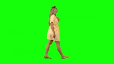 Bronzlaşmış sarışın kadın yeşil ekranda sakince yürüyor ve gülümsüyor. Krom anahtar, 4km 'lik atış. Profil görünümü.