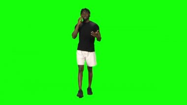 Afrikalı Amerikalı adam yürüyor ve konuşuyor. Green Screen, Chroma Key 'de cep telefonuyla. Ön görünüm.