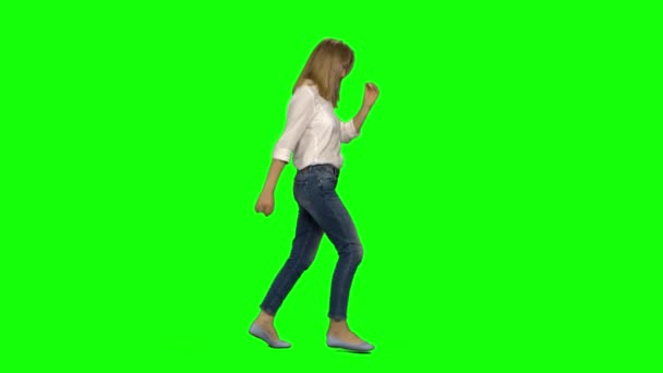 Blondine vrouw loopt met een glimlach op groen scherm. Chroma sleutel, 4K schot. Profielweergave. — Stockvideo