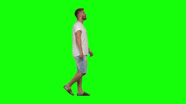 Barbudo cara calmamente andando no fundo tela verde. Chave Chroma, tiro 4K. Vista do perfil . — Vídeo de Stock