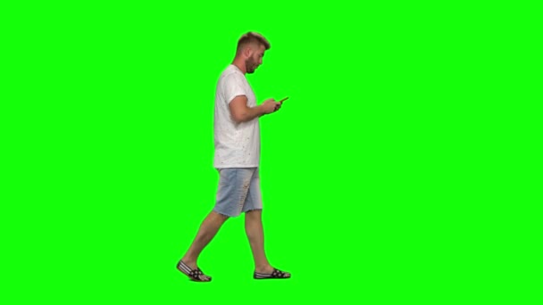 Бородатый парень спокойно ходит и отправляет сообщение на свой мобильный телефон на зеленый экран. Chroma key, 4k shot. Профиль — стоковое видео