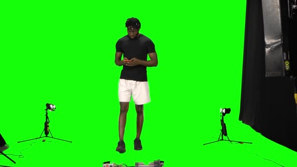 Bastidores filmagem vídeo afro-americano homem está andando e mensagens de texto vie seu telefone celular na tela verde. Vista frontal . — Vídeo de Stock