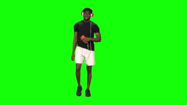 Afro-Amerikaanse man loopt in grote rode koptelefoon, kiest muziek op mobiele telefoon en beweegt naar ritme op Green Screen — Stockvideo