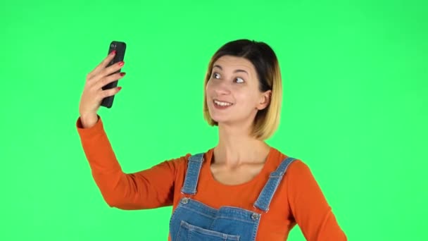 Молода жінка робить селфі на мобільному телефоні, а потім дивиться фотографії на зеленому екрані — стокове відео