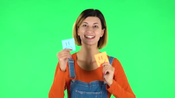 Девушке с бумажной палочкой, выражающей ужасное настроение, нужен другой, выражающий хорошее настроение. Зеленый экран — стоковое видео