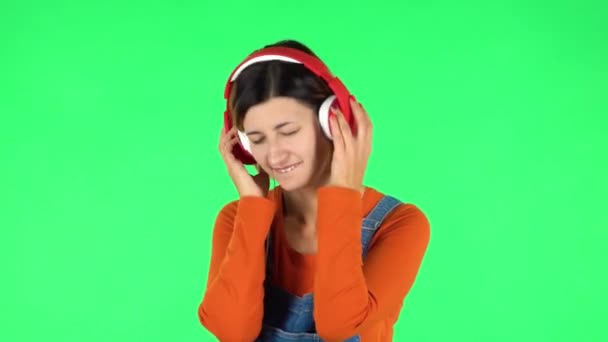 陽気な女の子は踊り、大きな赤いヘッドフォンで音楽を楽しんでいます。緑の画面 — ストック動画