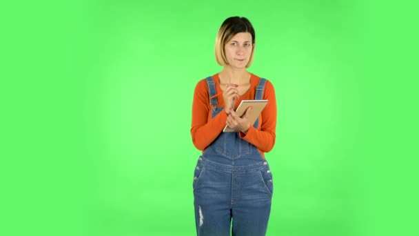 A menina está e pensa, então atentamente escreve com lápis no caderno. Tela verde — Vídeo de Stock