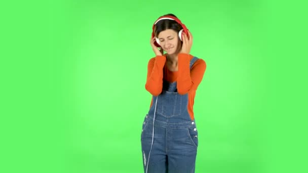 Chica alegre bailando y disfruta de la música en grandes auriculares rojos. Pantalla verde — Vídeos de Stock