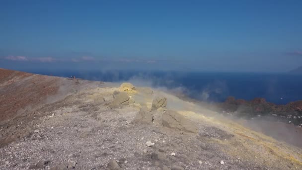 Gas volcánico saliendo a través de fumarolas en el cráter Fossa de la isla Vulcano. Gente caminando por una cresta humeante. Islas Lipari. Cielo azul. Sicilia, Italia — Vídeo de stock
