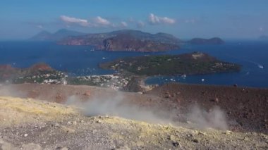 Volkanik gaz, Vulcano adasındaki Fossa kraterinden çıkıyor. İnsanlar dumanı tüten tepenin yanından geçiyor. Lipari Adaları. Mavi gökyüzü. Sicilya, İtalya