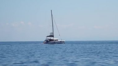 Akdeniz 'de yüzen insanlarla dolu beyaz yelkenli bir tekne. Lipari Adaları. Sicilya, İtalya. Ufuk, mavi gökyüzü