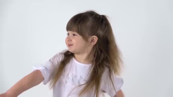 Симпатична маленька дівчинка з радістю гризе на білому тлі, а потім складає долоні перед нею. Близько. Повільний рух — стокове відео
